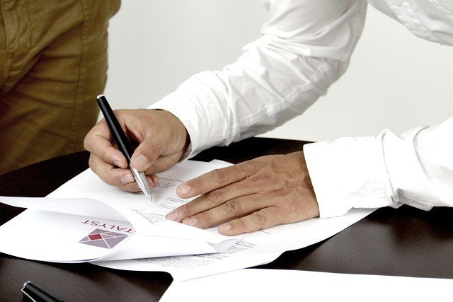 Close-up of person signing property documents with a pen at a desk.