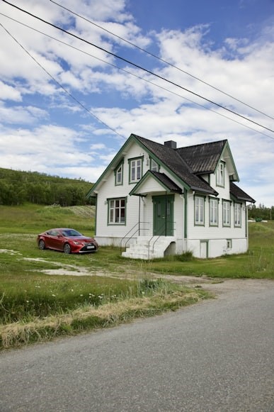 White house with green trim in quiet rural area, red car parked outside